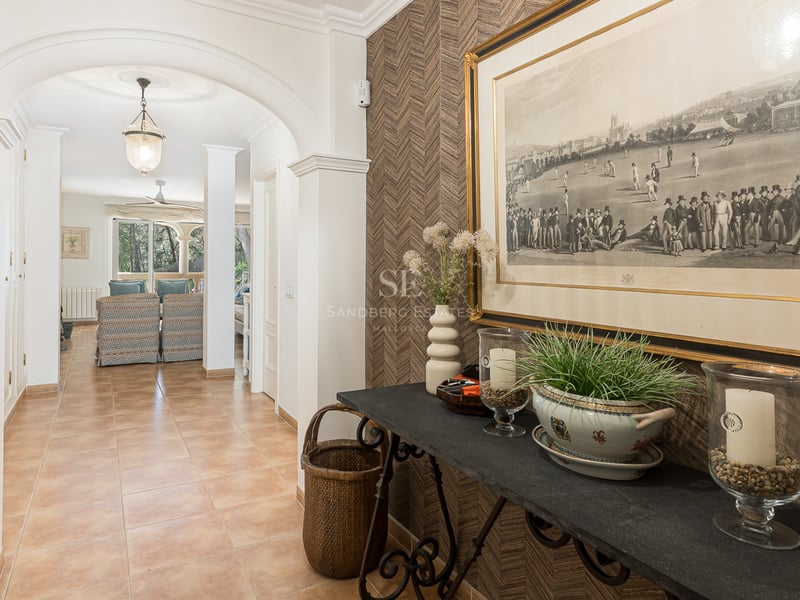 Bright hallway with terracotta tiles, white archways, and a decorated console table leading towards the living area.