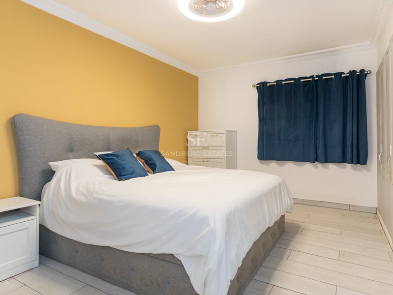 Une chambre lumineuse avec lit gris, mur jaune, placards blancs et rideaux bleu foncé.