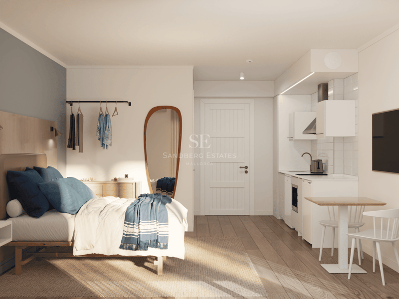 Studio lumineux avec lit aux accents bleus, grand miroir et kitchenette blanche moderne.