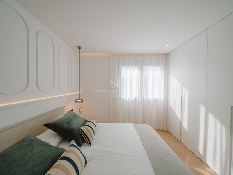 Chambre lumineuse avec panneaux blancs, lit aux coussins verts, parquet en chevrons et placards intégrés.