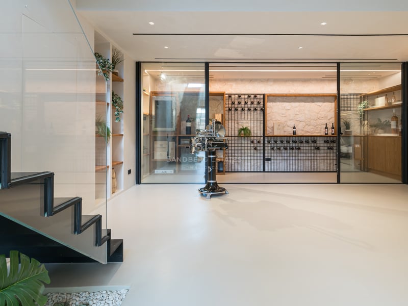 Modern vinkällare i glas med stenvägg, platsbyggda hyllor och minimalistisk trappa i lyxvilla.