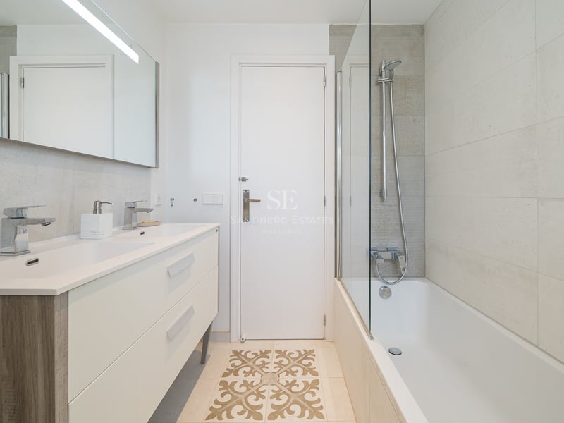 Modern bathroom featuring a cream double vanity, bathtub with glass screen, and decorative floor tile detail.