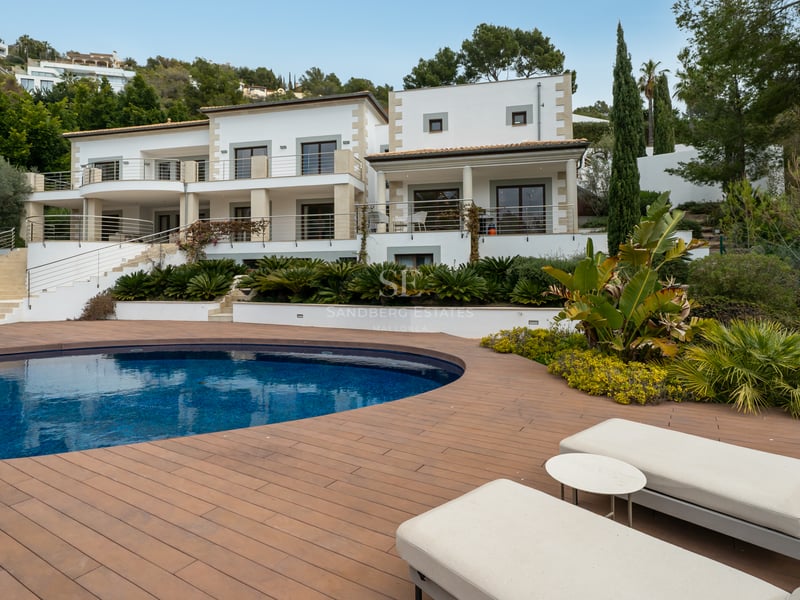 Villa de luxe blanche avec piscine incurvée, terrasse en bois et bains de soleil dans un cadre paysager.