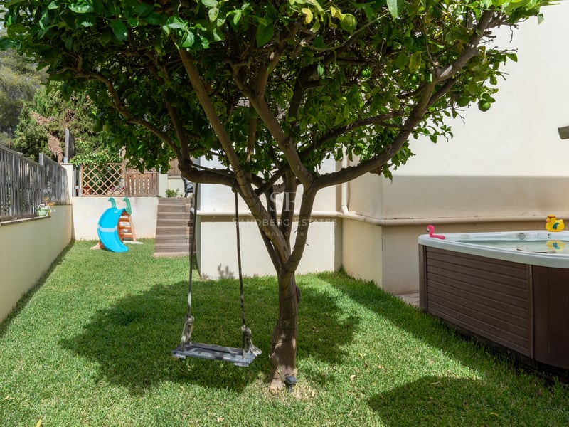 Jardin avec pelouse, balançoire dans un arbre, toboggan bleu et jacuzzi extérieur habillé de bois.