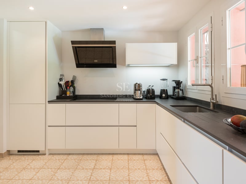 Contemporary kitchen featuring white handleless cabinets, dark stone countertops, and decorative patterned floor tiles.