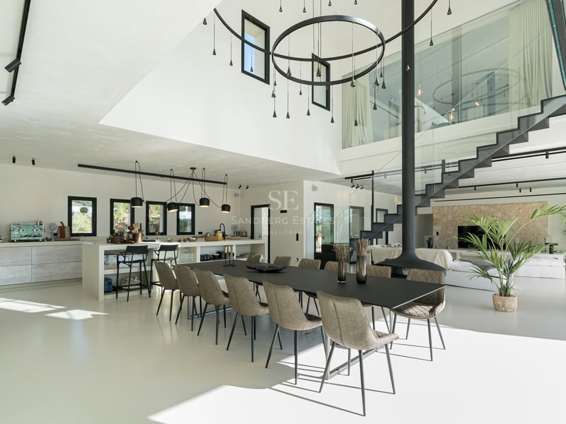 Modern matsal med svart långbord, hängande öppen spis och entresolplan i glas.