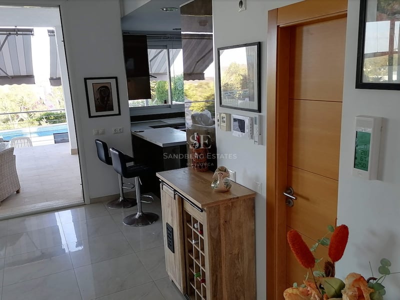 Vue intérieure d'un espace de vie moderne avec cave à vin, ouvrant sur une terrasse ensoleillée et une piscine.