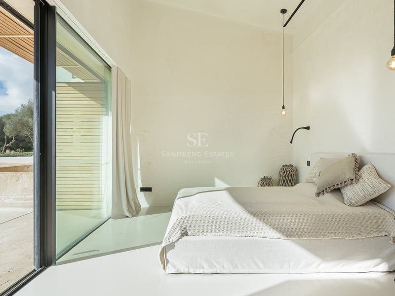 Ljust minimalistiskt sovrum med vit säng, stora glaspartier och privat balkong.