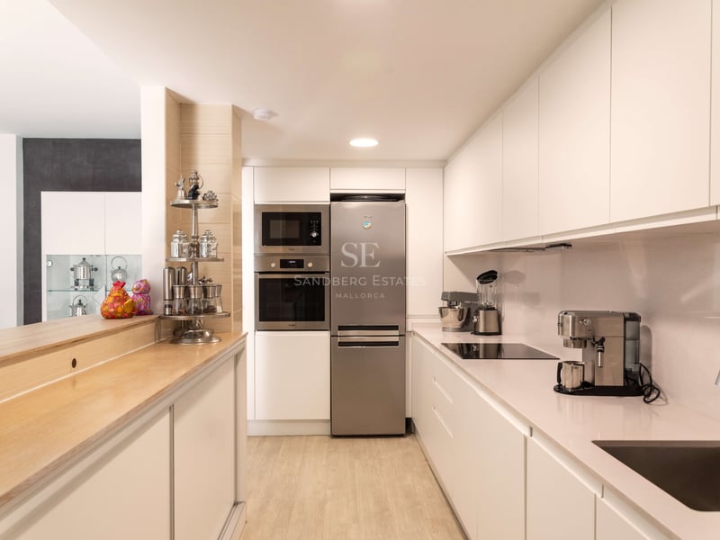 Saubere, moderne Küche mit weißen Schränken, Edelstahlgeräten und einer Frühstücksbar aus hellem Holz.