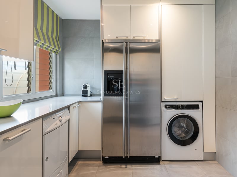 Modern laundry area featuring a large stainless steel refrigerator, washing machine, and white cabinetry against grey tiles.