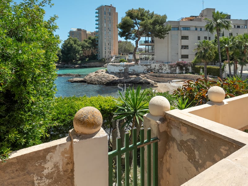 Utsikt över en turkos vik och stenig kustlinje från en medelhavsterrass med stenmurar.