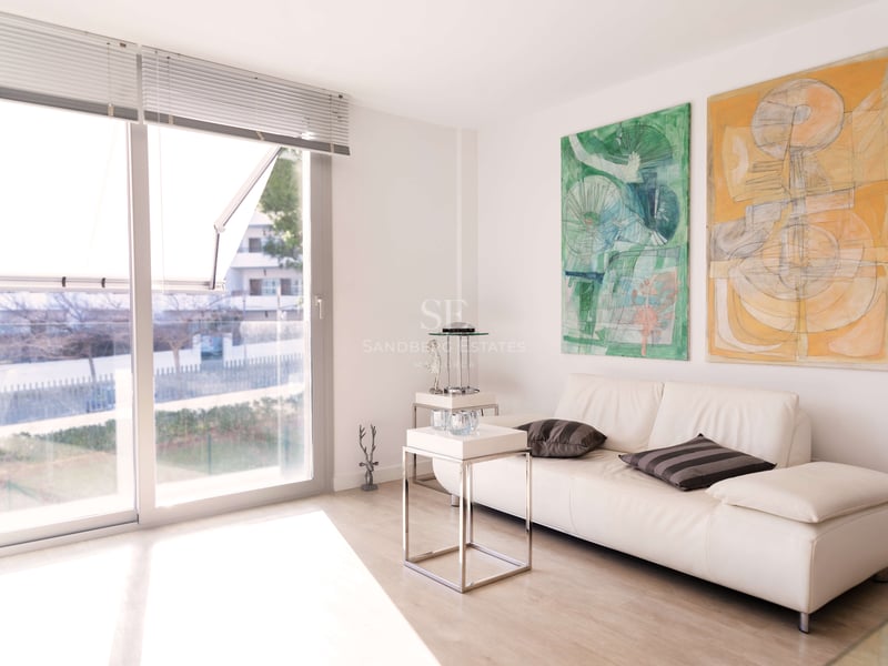 Helles Wohnzimmer mit weißem Ledersofa, zwei großen abstrakten Gemälden und bodentiefen Fenstern.