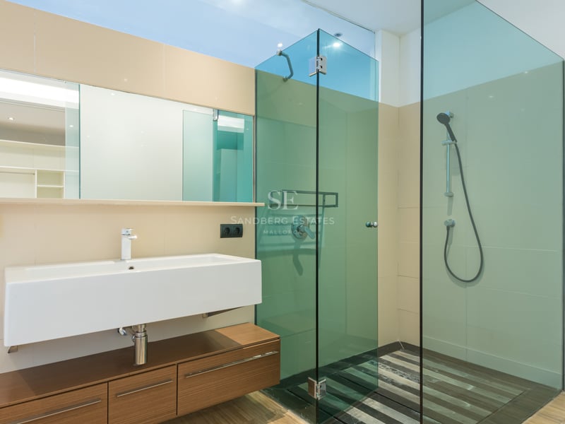 Modernt badrum med ett rektangulärt tvättställ, svävande träkommod och duschkabin i tonat glas.