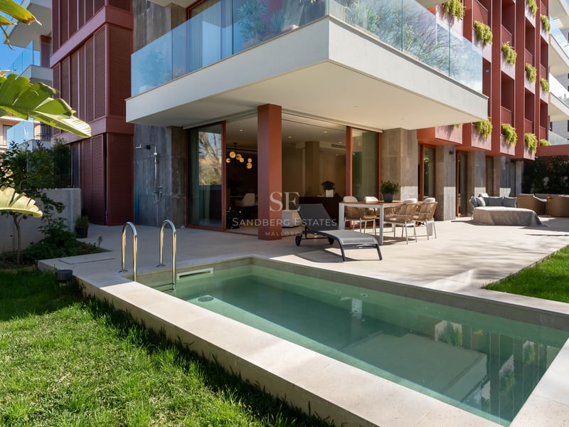 Luxury terrace with private plunge pool, outdoor dining set, sun lounger, and green lawn by a modern apartment building.