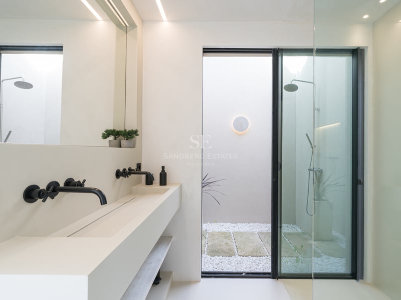 Modernt vitt dubbelhandfat med mattsvarta kranar och walk-in-dusch som vetter mot en innergård med stenar.