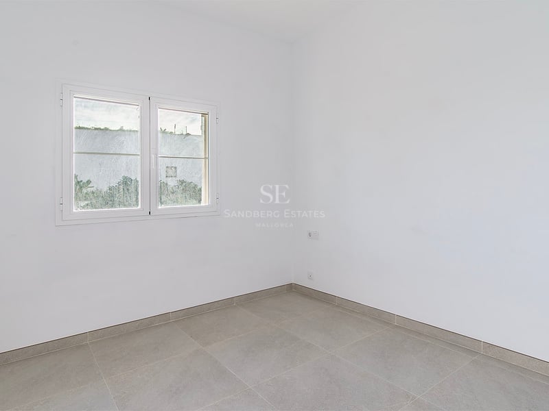 Tomt vitt rum med grå stengolv, tvåglasfönster och ett väggmonterat element.