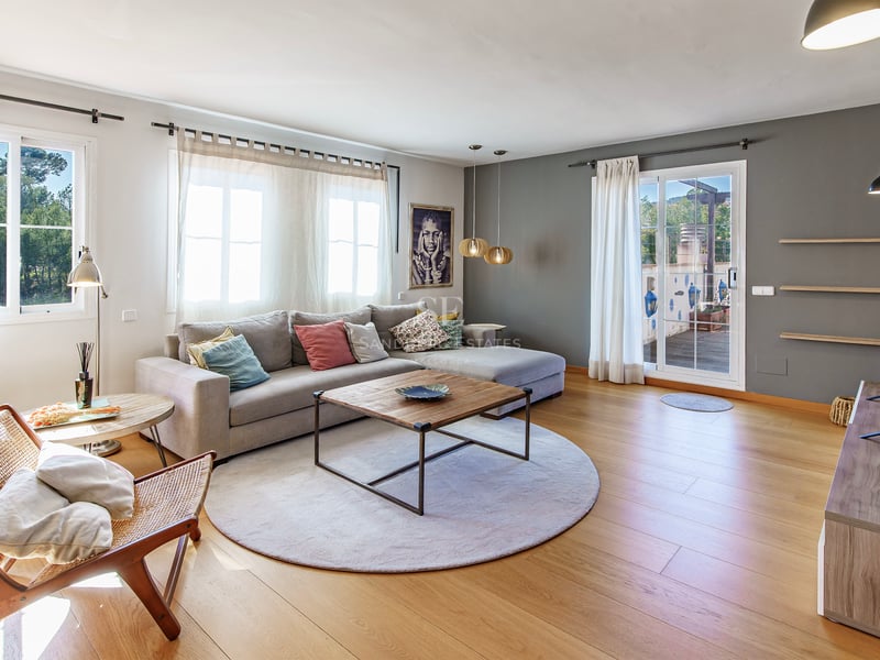 Ljust vardagsrum med grå hörnsoffa, ekparkett och glasdörr som leder till en solig terrass.
