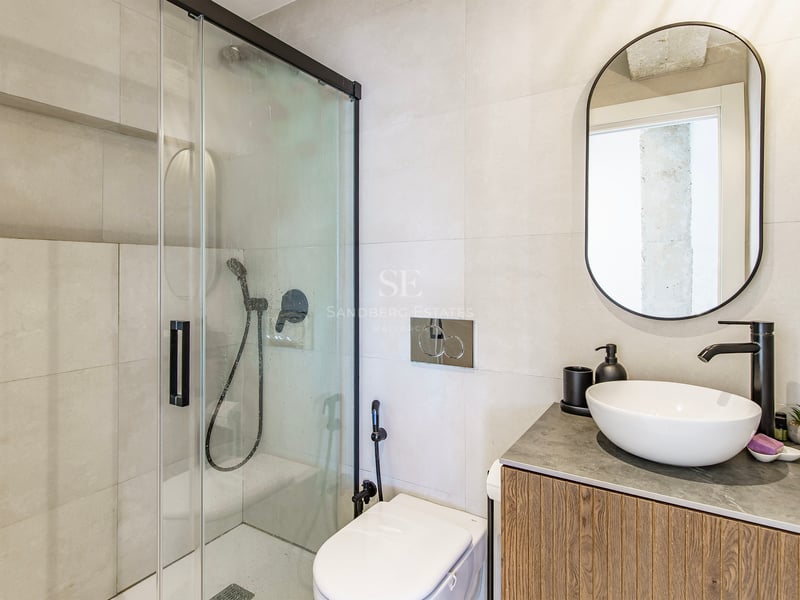 Salle de bain contemporaine avec douche vitrée, robinetterie noire, meuble en bois et miroir ovale.