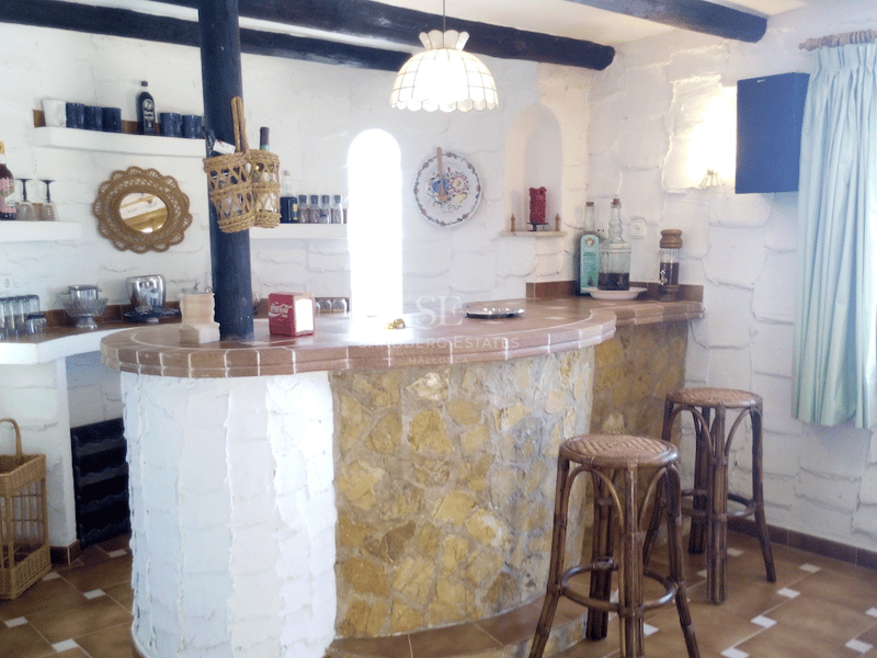 Un bar interior con base de piedra curva, encimera de baldosas de terracota y vigas de madera oscura en el techo.