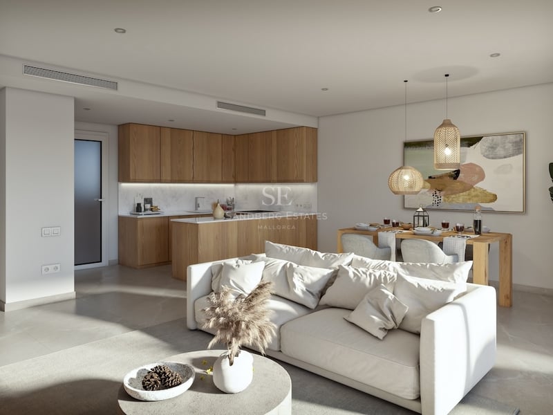 Bright open-plan living space with a white sofa, wooden kitchen cabinets, and a dining area with woven pendant lights.