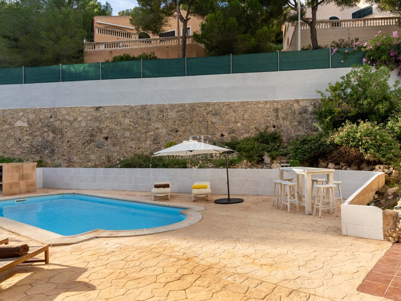Piscine privée avec chaises longues, parasol blanc et mur en pierre rustique en arrière-plan.