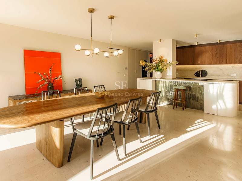 Großzügiges Esszimmer mit ovalem Holztisch, Designer-Pendelleuchte und moderner Küche im Hintergrund bei Sonnenlicht.