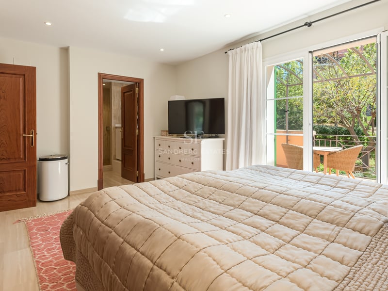 Bright bedroom featuring quilted bedding, wooden doors, and sliding glass doors to a terrace with wicker furniture.