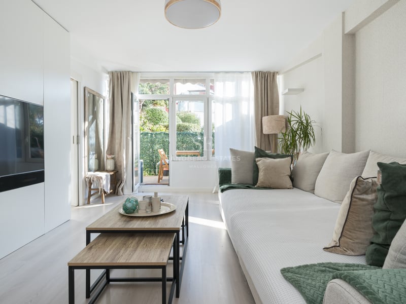 Bright living room featuring a large beige sofa, wooden coffee tables, and glass doors opening to a green terrace.
