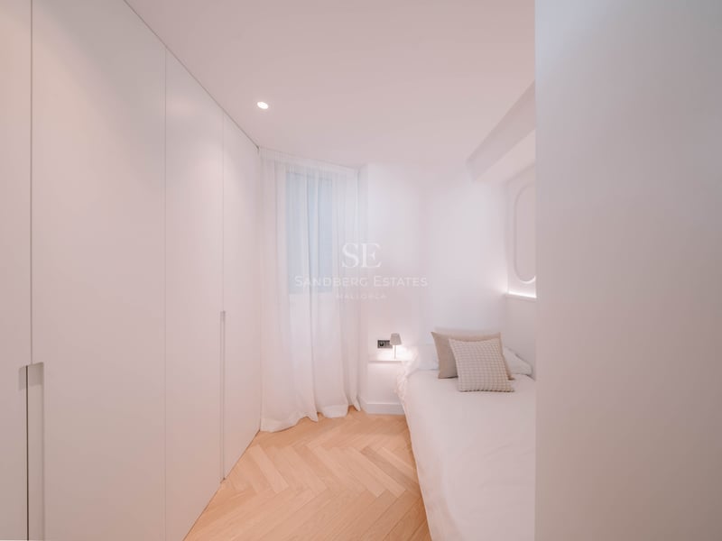 Chambre lumineuse avec placards blancs intégrés, parquet en chevrons et un lit simple avec éclairage doux.