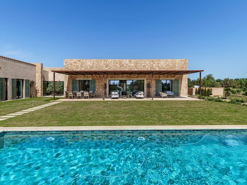 Luxusvilla-Exterieur mit türkisfarbenem Pool, Rasenfläche und Natursteinfassade unter klarem blauem Himmel.