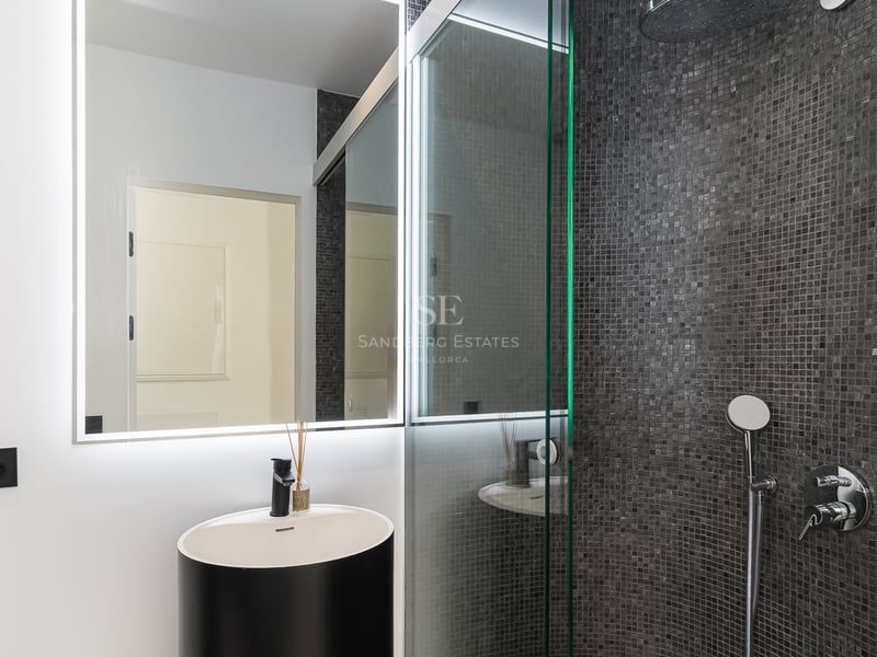 Modernt badrum med svart cylindriskt tvättställ, LED-spegel och dusch med mörkgrå mosaik.