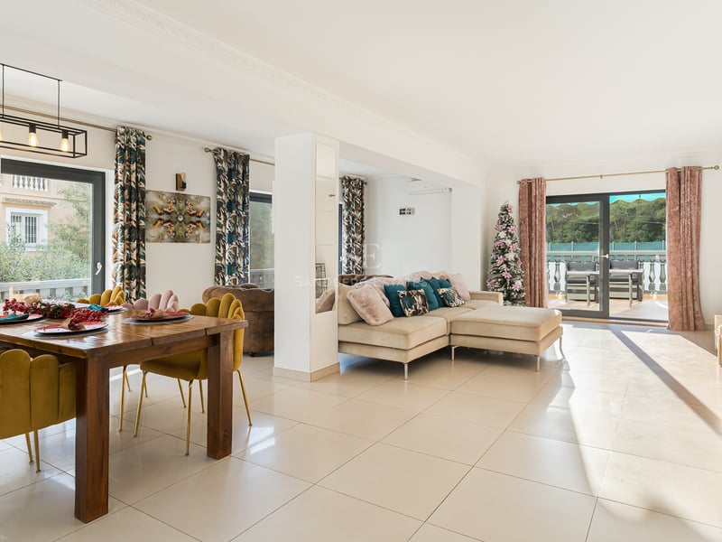 Espace de vie lumineux avec chaises en velours moutarde, canapé beige et grandes baies vitrées ouvrant sur une terrasse.