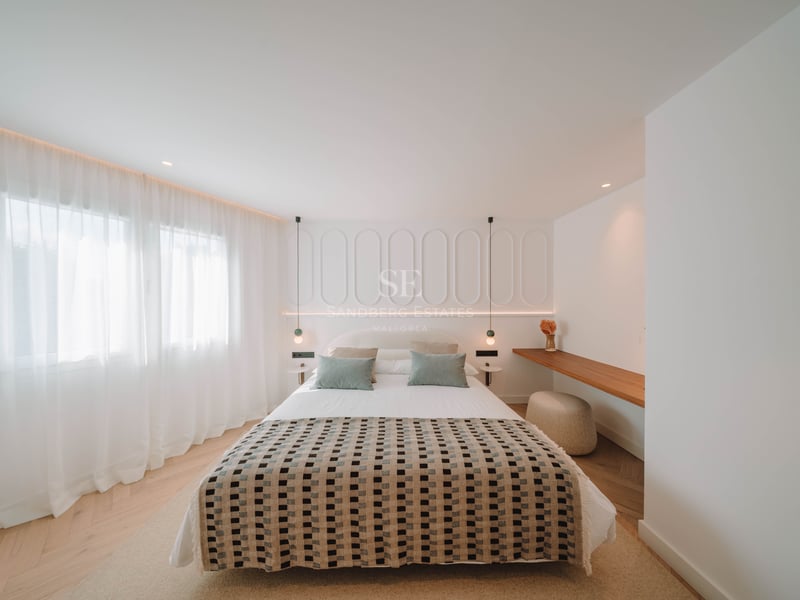 Chambre moderne lumineuse avec couvre-lit à motifs, mur de tête de lit à panneaux blancs et parquet en chevrons.