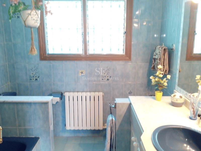 Badrum med ljusblått kakel, bänkskiva i vit marmor med blått tvättställ, element och fönster med träram.