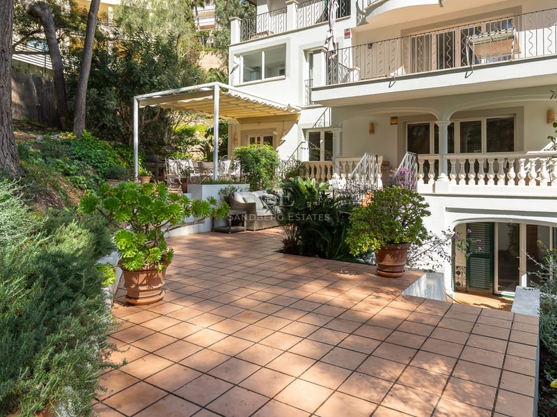 Spacious multi-level terracotta terrace surrounded by mature Mediterranean plants and a white villa facade.
