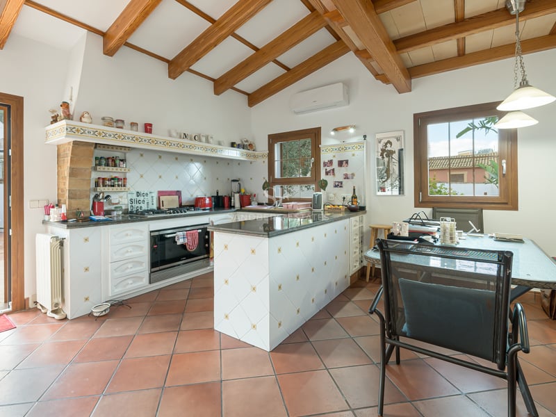 Mediterranean kitchen featuring terracotta floors, wooden ceiling beams, a white island, and a dining area by the terrace.