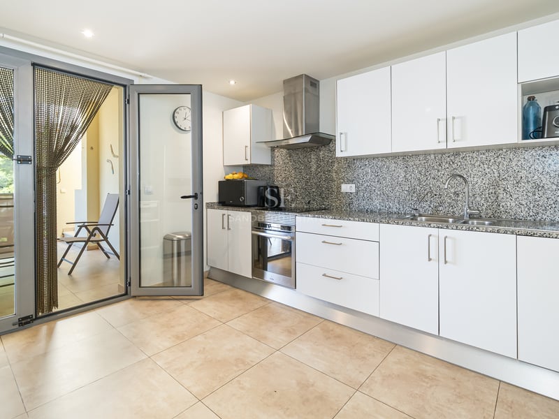 Modernt vitt kök med bänkskivor i granit och glasdörr ut mot en möblerad terrass.