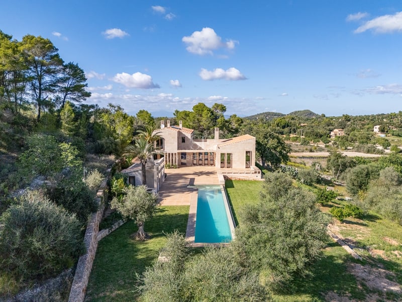 Vue d'une villa moderne en pierre avec une longue piscine turquoise entourée d'une végétation méditerranéenne luxuriante.