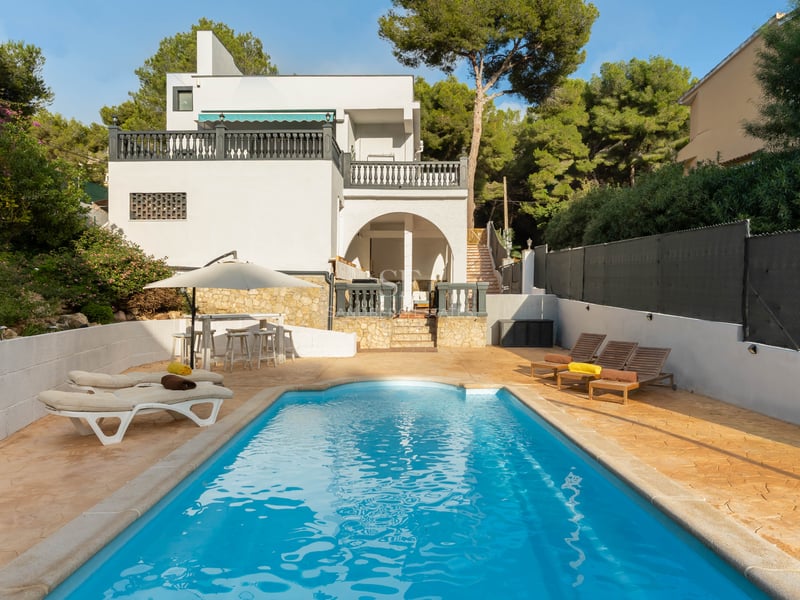 Piscine bleue entourée d'une terrasse en pierre avec transats et une villa blanche en arrière-plan.