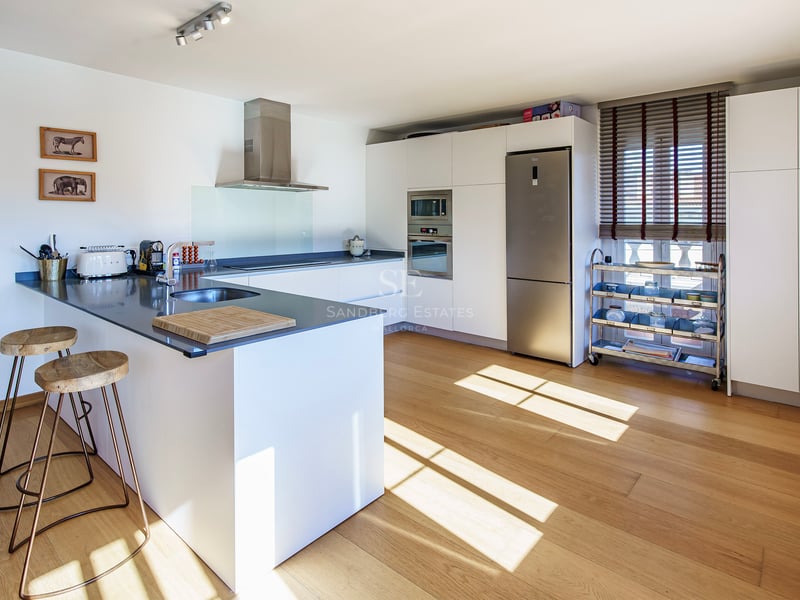 Modernt designat kök med vit köksö, grå bänkskiva, trägolv och vitvaror i rostfritt stål.