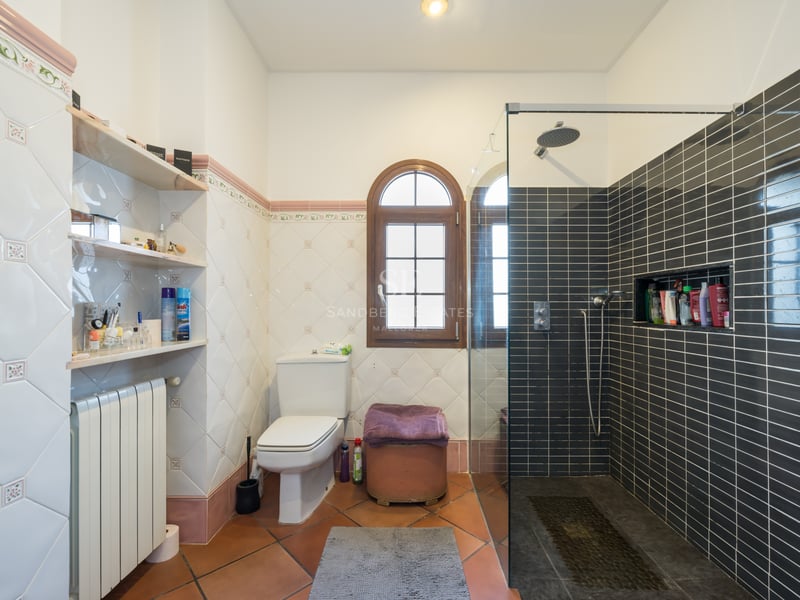 Bathroom featuring terracotta floors, decorative wall tiles, an arched wooden window, and a modern glass walk-in shower.