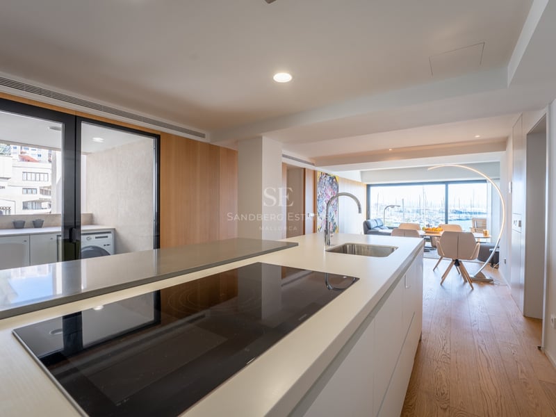 Modern vit köksö med induktionshäll och diskho, med utsikt över en matplats och hamnen.