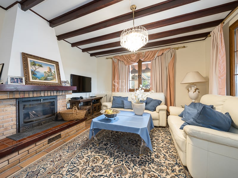 Salon avec cheminée en briques, poutres apparentes, canapés en cuir crème et lustre en cristal.