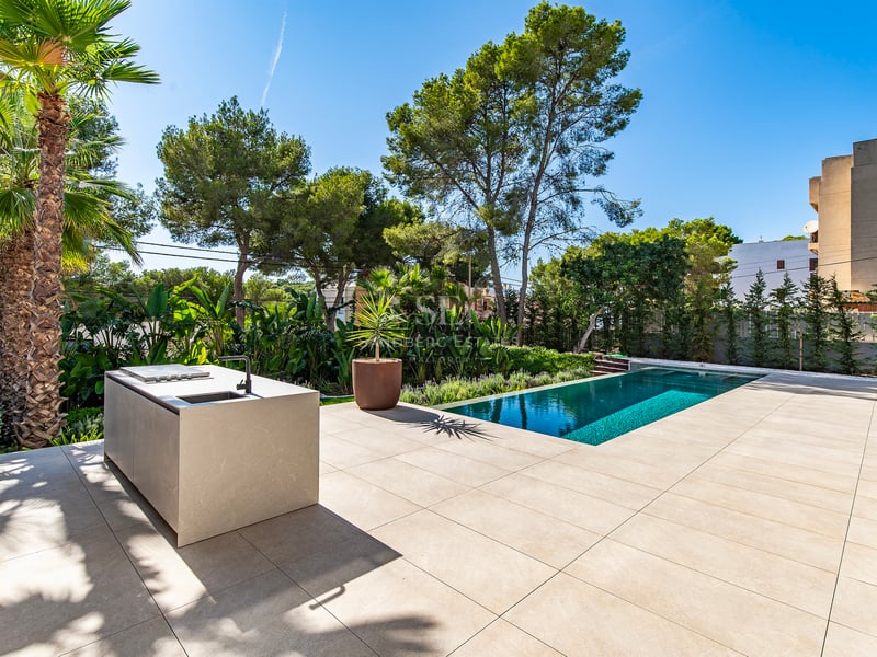 Terrasse en pierre avec îlot de cuisine minimaliste à côté d'une piscine turquoise et jardins tropicaux.