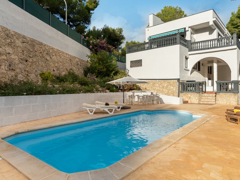 Piscine rectangulaire à l'eau turquoise entourée d'une terrasse en pierre, de chaises longues et d'une villa blanche.