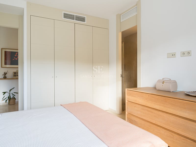 Ljust sovrum med krämfärgade garderober, träbyrå och säng med pastellrosa pläd.