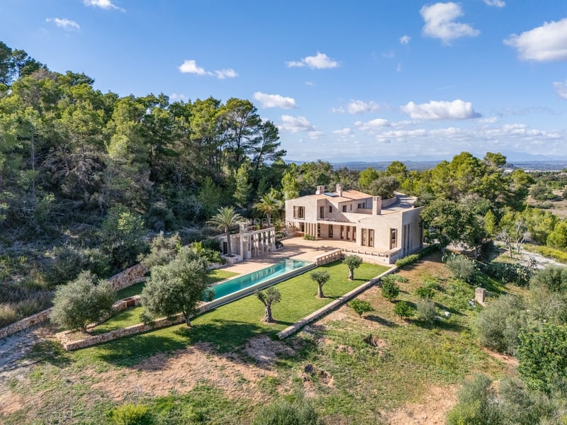 Vue aérienne d'une villa de luxe en pierre avec piscine turquoise entourée d'oliviers et de forêt.