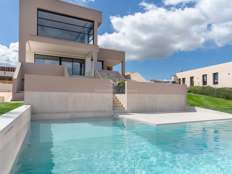 Türkisfarbener Pool im Vordergrund vor einer zeitgenössischen beigen Villa unter blauem Himmel.