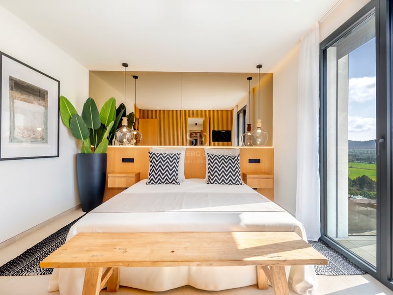 Chambre contemporaine lumineuse avec tête de lit en bois, suspensions en verre et baies vitrées ouvrant sur la nature.