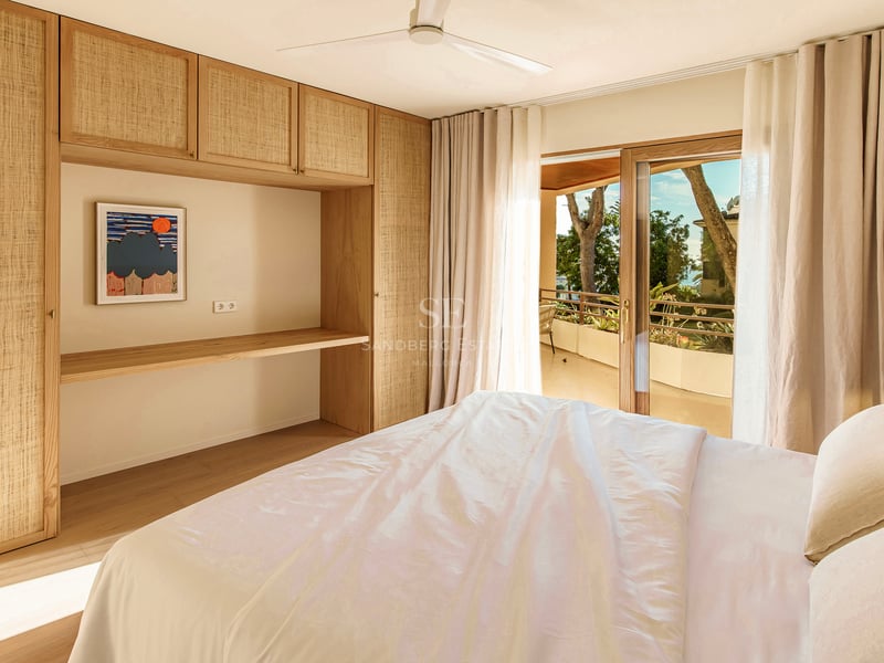 Helles Schlafzimmer mit Einbauschränken aus hellem Holz, Schreibtisch und Schiebetüren zu einer sonnigen Terrasse.